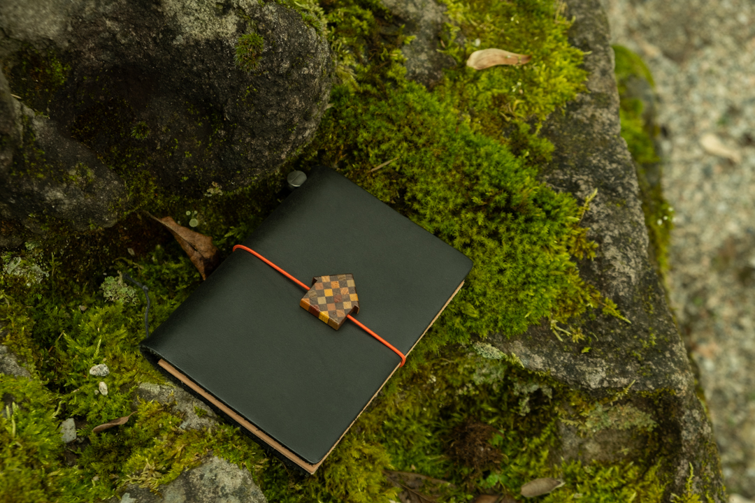 TRAVELER'S notebook with Luthier House Charm against the moss.