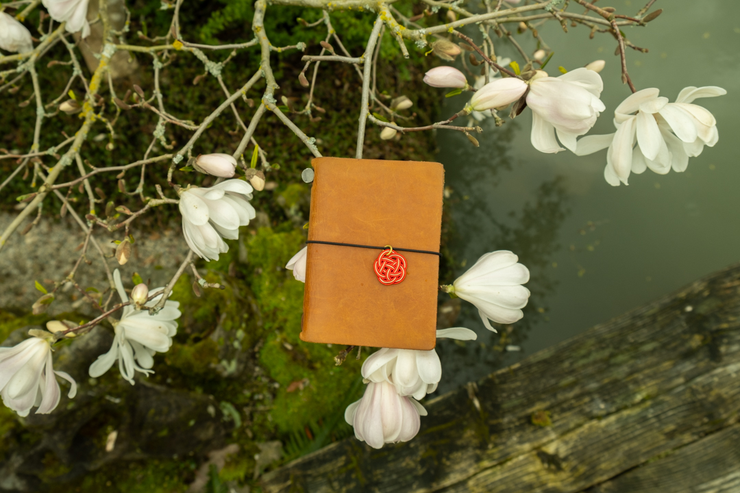 TRAVELER'S notebook Passport Size with MIZUHIKI Charm positioned with magnolia flowers.