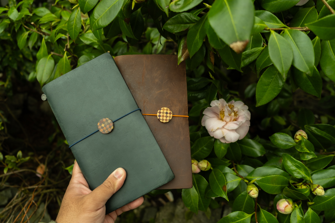 TRAVELER'S notebook with YOSEGI Charms against green leaves.