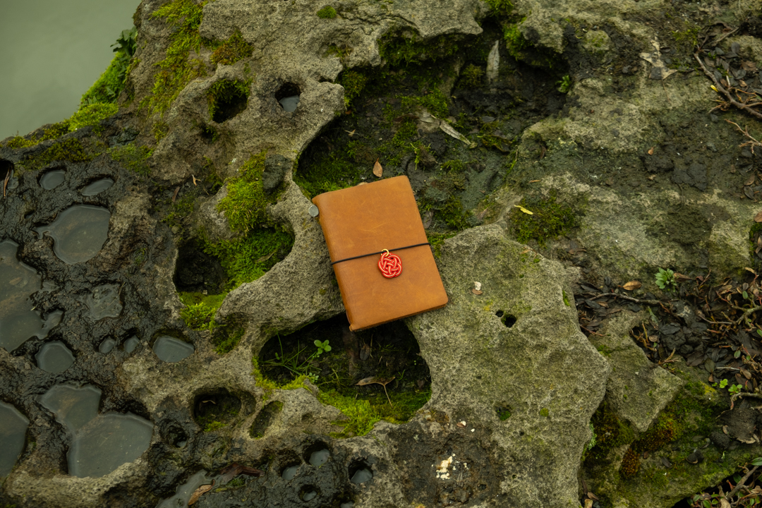 TRAVELER'S notebook Passport Size with red MIZUHIKI Charm on the ground.