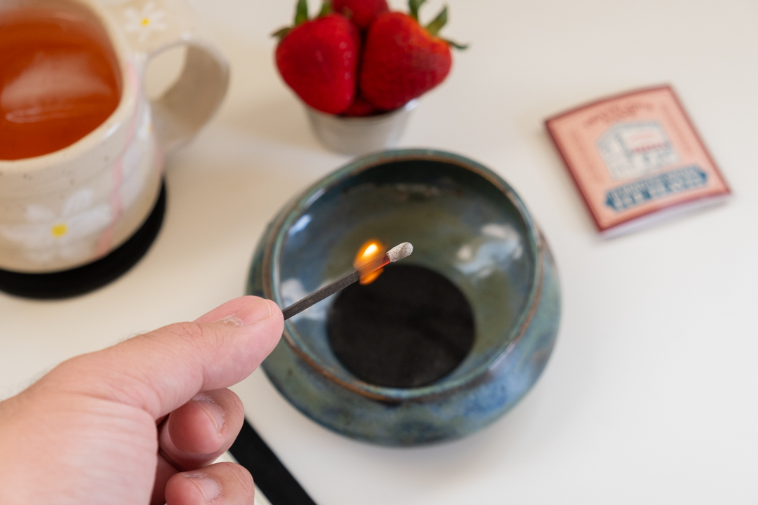 Striking a hibi incense match to light the incense near a ceramic bowl.