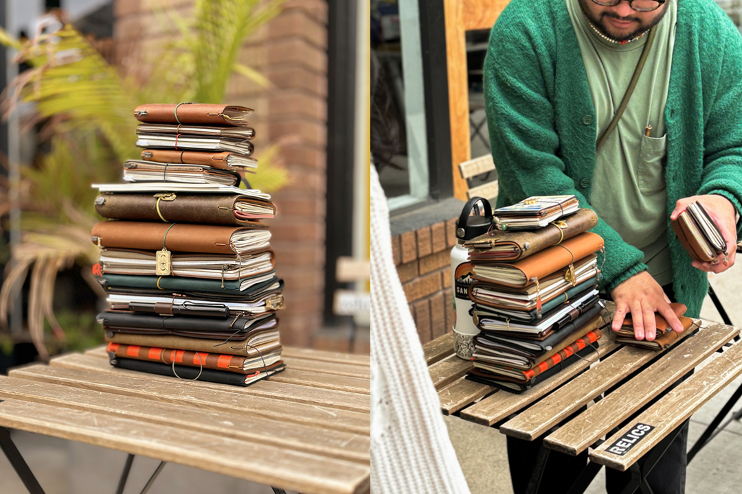 A stack of TRAVELER'S notebooks on a wooden table and a man stacking the notebooks on the wooden table.