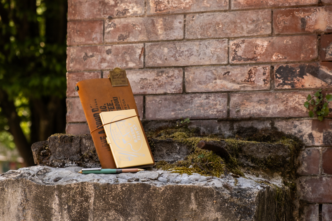 TRAVELER'S notebook with TRC USA x Art Toolkit palette against a red brick wall.