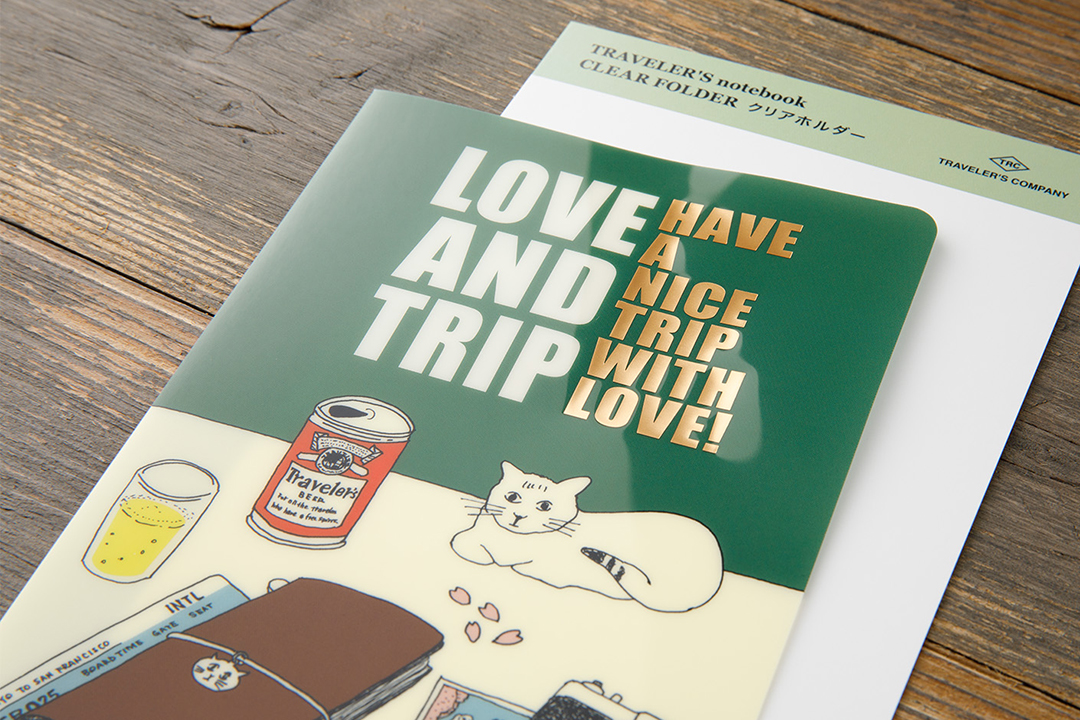 Close up of the green clear folder with illustrations of cat, beer, and TRAVELER'S notebook from DIARY 2025. 