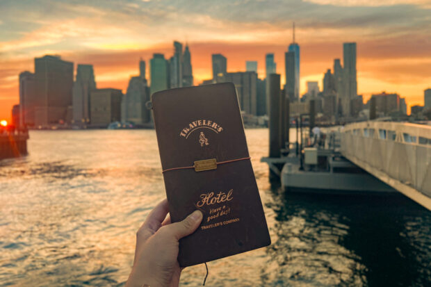 TRAVELER'S notebook in front of New York sky line at sunset.