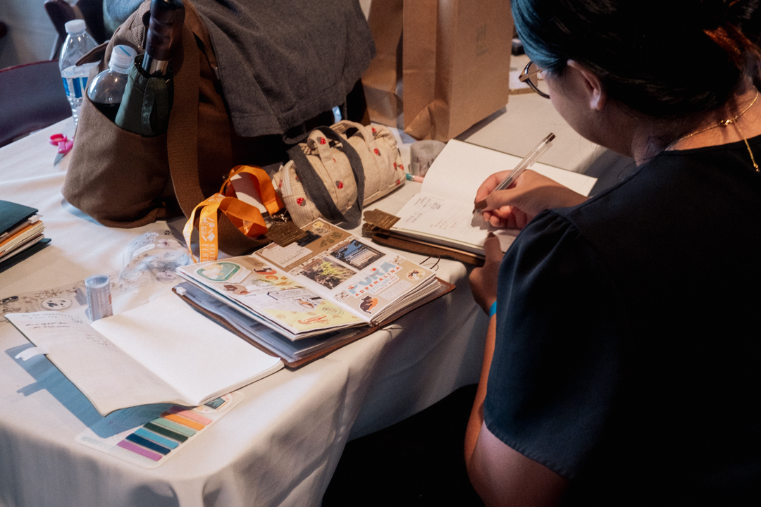 TRAVELER'S notebook user journaling at a white table surrounded by stationery.