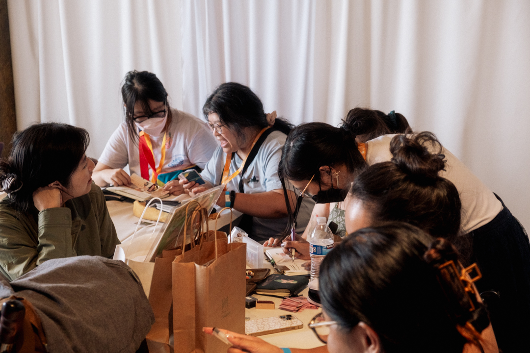 TRAVELER'S notebook users journaling together at a white table surrounded by stationery.