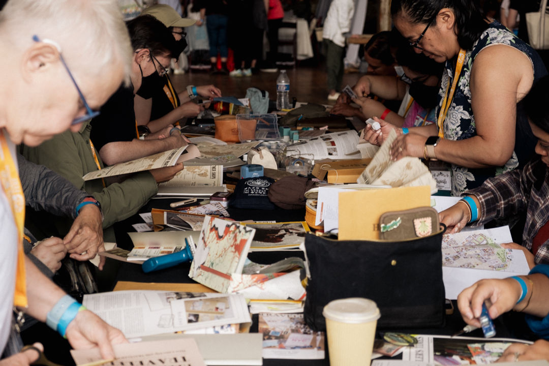 TRAVELER'S notebook users at a workshop journaling, collaging, and creating art together at a white table.