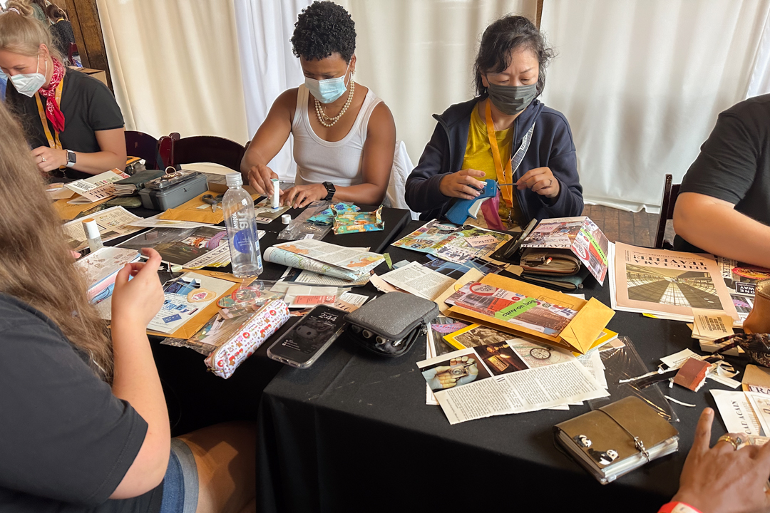 TRAVELER'S notebook users at a workshop journaling, collaging, and creating art together at a white table.