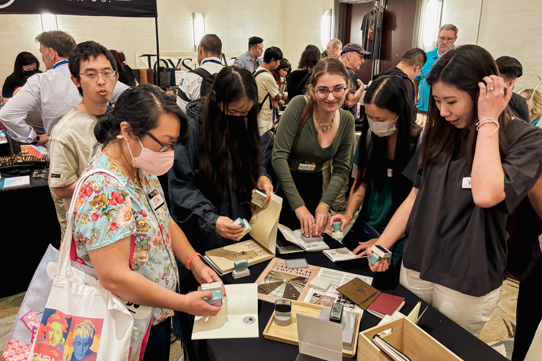 An enthusiastic crowd at the TRAVELER'S COMPANY pop-up table with stamps.