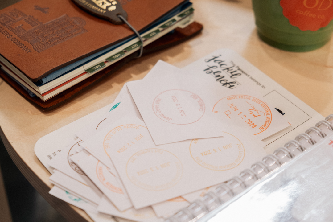 National Park stamps on little sheets of paper on a wooden table beside leather journals.