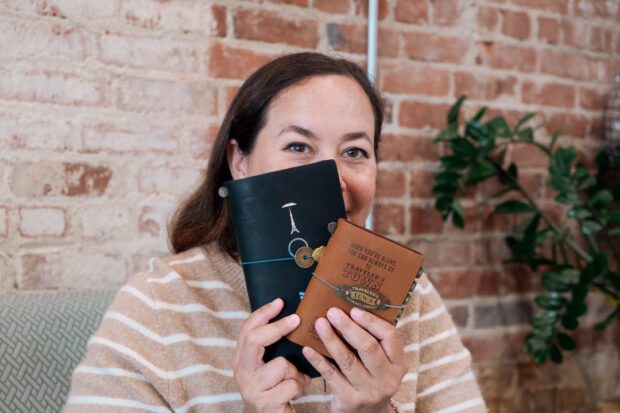 Portrait of Jackie Benefield holding two TRAVELER'S notebooks which are covering half of her face.