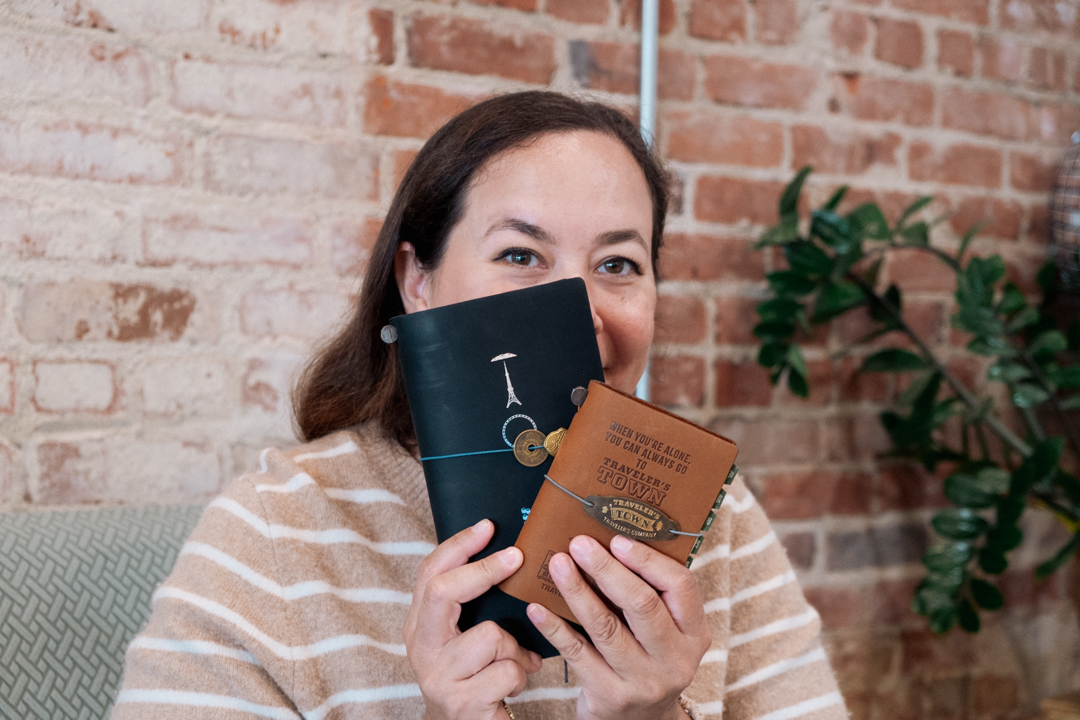 Portrait of Jackie Benefield holding two TRAVELER'S notebooks which are covering half of her face.