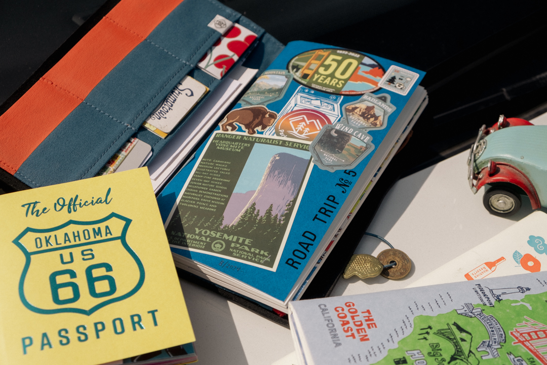 A TRAVELER'S notebook open to show a notebook insert decorated with Road Trip stickers beside other notebooks.