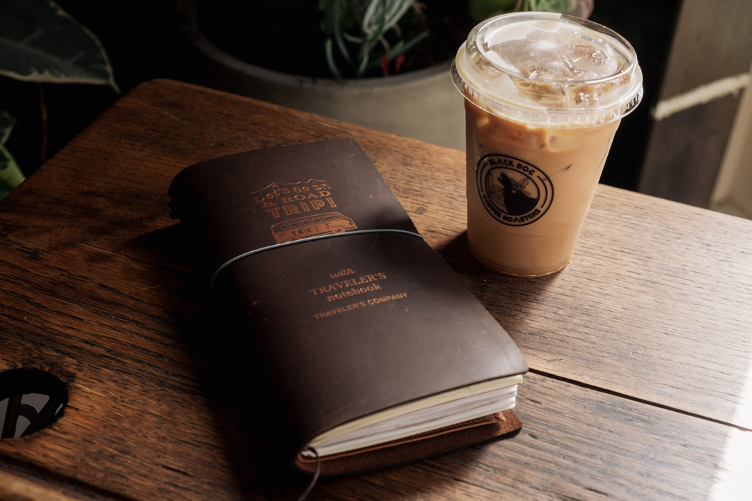 TRAVELER'S notebook next to an iced coffee by Black Dog Coffee Roasters.