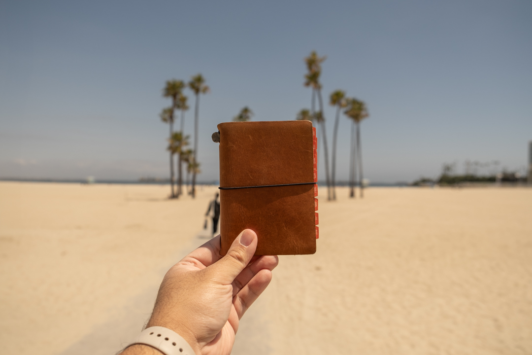 A TRAVELER'S notebook Passport Size held against the sandy beaches of Long Beach.