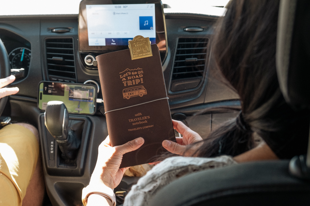 Woman holding a TRAVELER'S notebook USA Road Trip in the passenger seat.