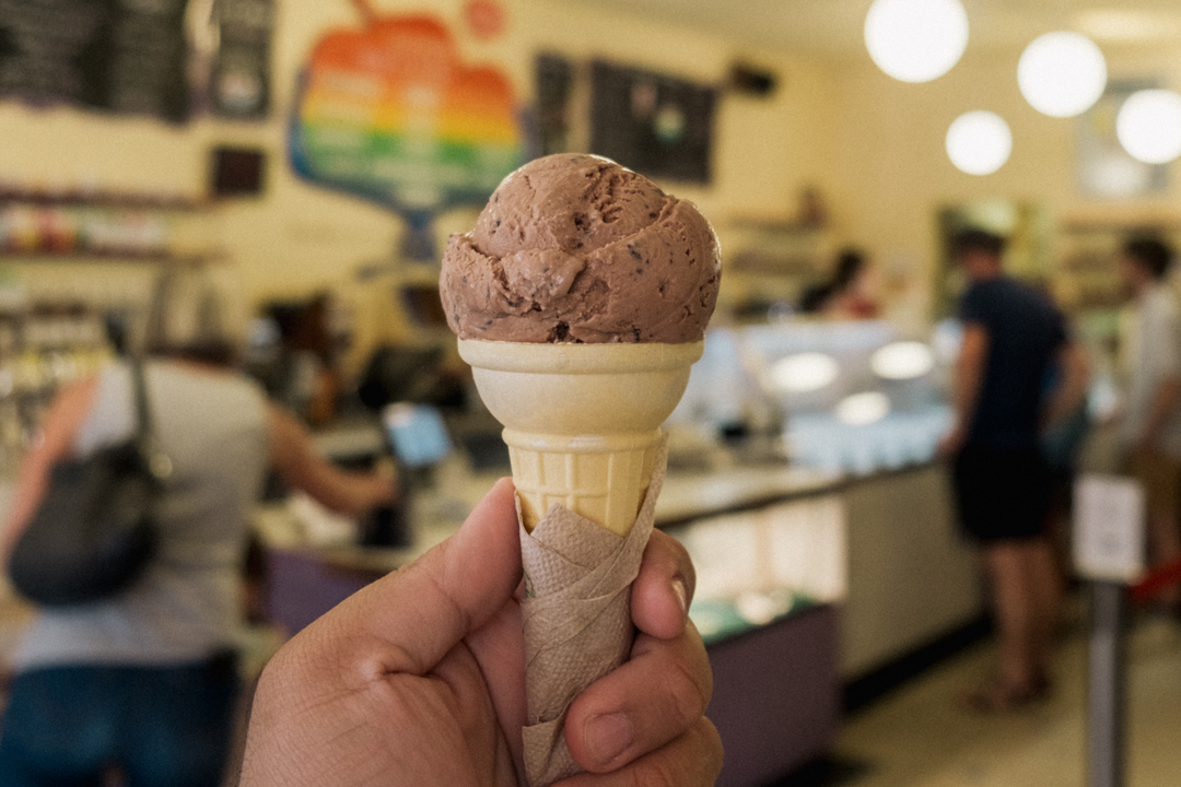 A hand holding up a scoop of ice cream against the ice cream parlor.