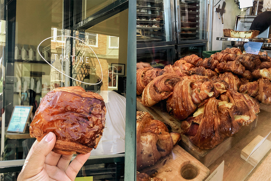 A hand holding up a pastry by Tartine Bakery.