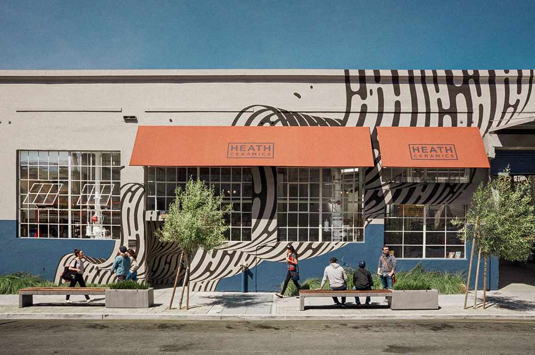 The exterior view of Heath Ceramics with a vibrant mural on the wall.