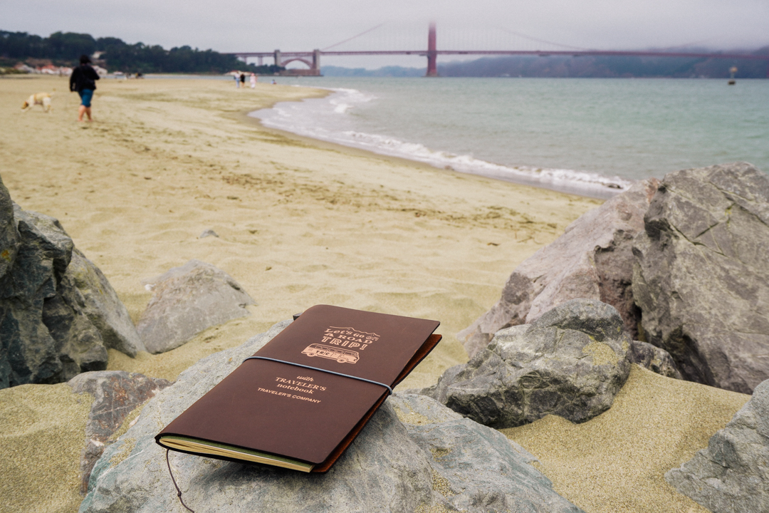 TRAVELER'S notebook USA Road Trip Edition on a rock at the beach with Golden Gate Bridge on the horizon.