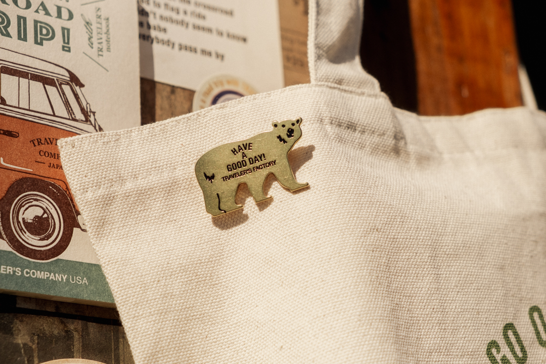 TRAVELER'S FACTORY Brass Bear Badge pinned on a canvas tote bag.