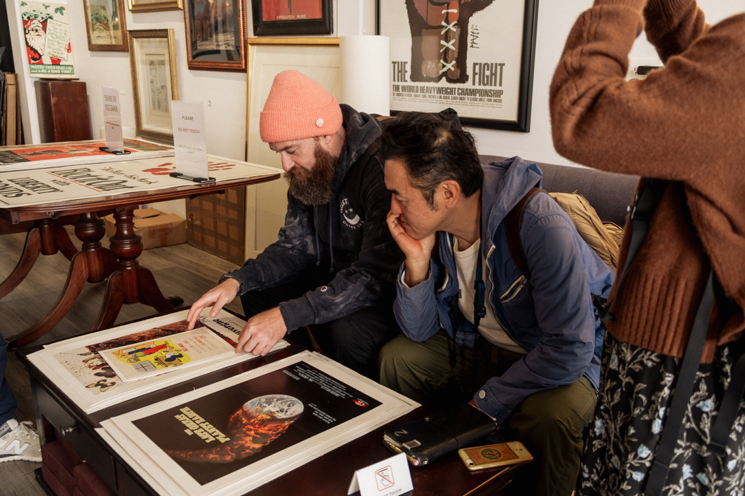 Two men looking at vintage art prints while sitting down on a sofa.