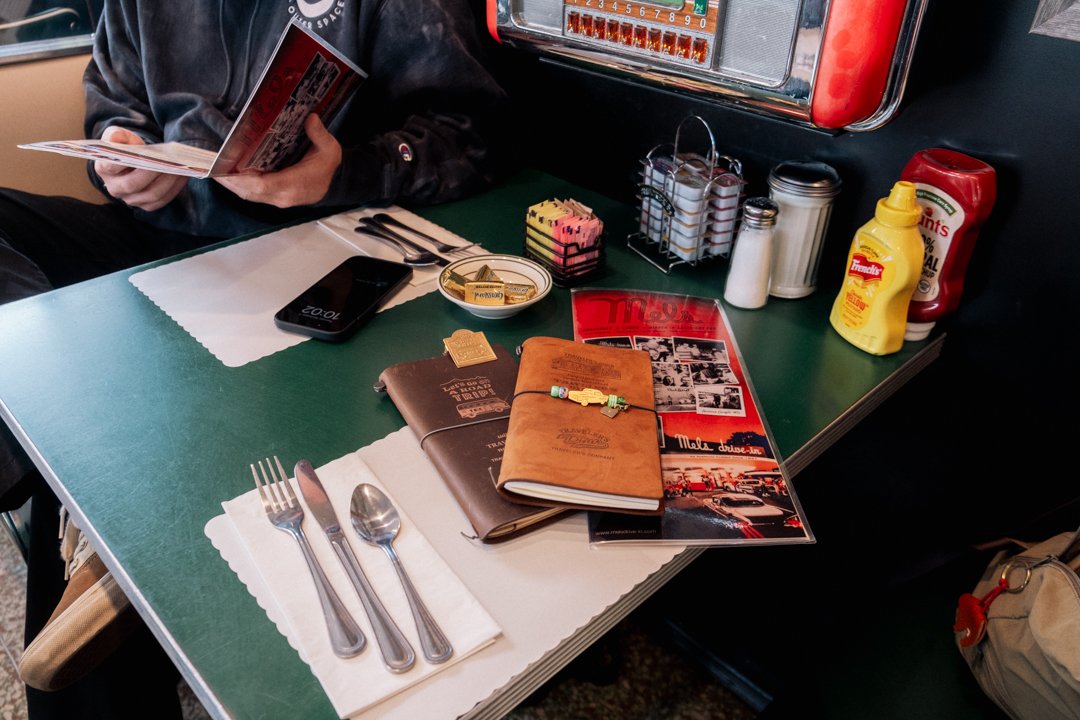 TRAVELER'S notebooks on top of the Mel's Diner Menu at a 2-person table booth.