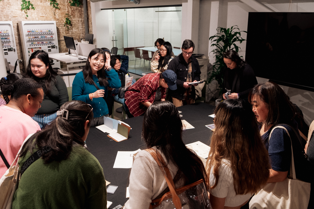 People huddled over a table filled with ink stamps, with people stamping their notebooks.