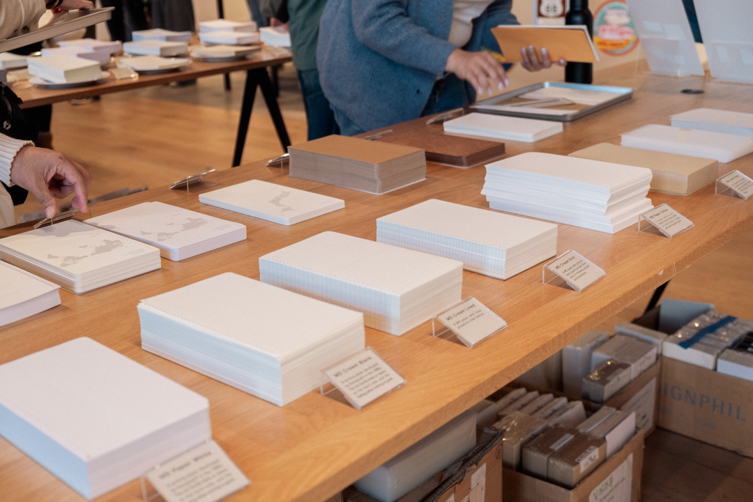 Stacks of neutral-colored papers on wooden table with labels in front of each stack.