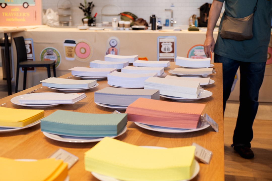 Stacks of different color papers on wooden table with labels in front of each stack.