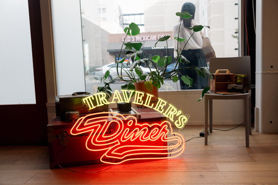 Neon sign against vintage luggage and a plant.