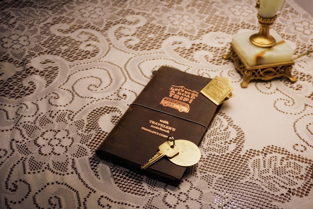 TRAVELER'S notebook on a table with a vintage lace table cloth and vintage hotel room key.