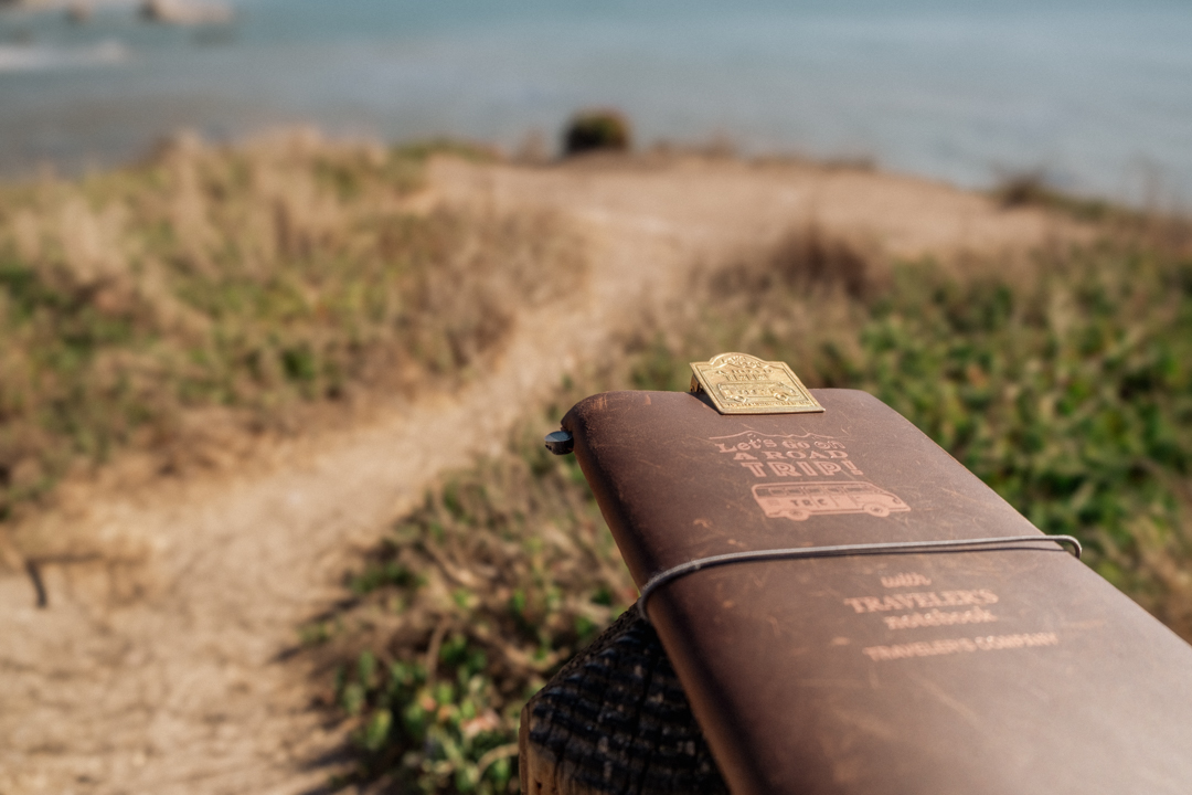 A TRAVELER'S notebook resting on a post in front of a scenic oceanside cliff.