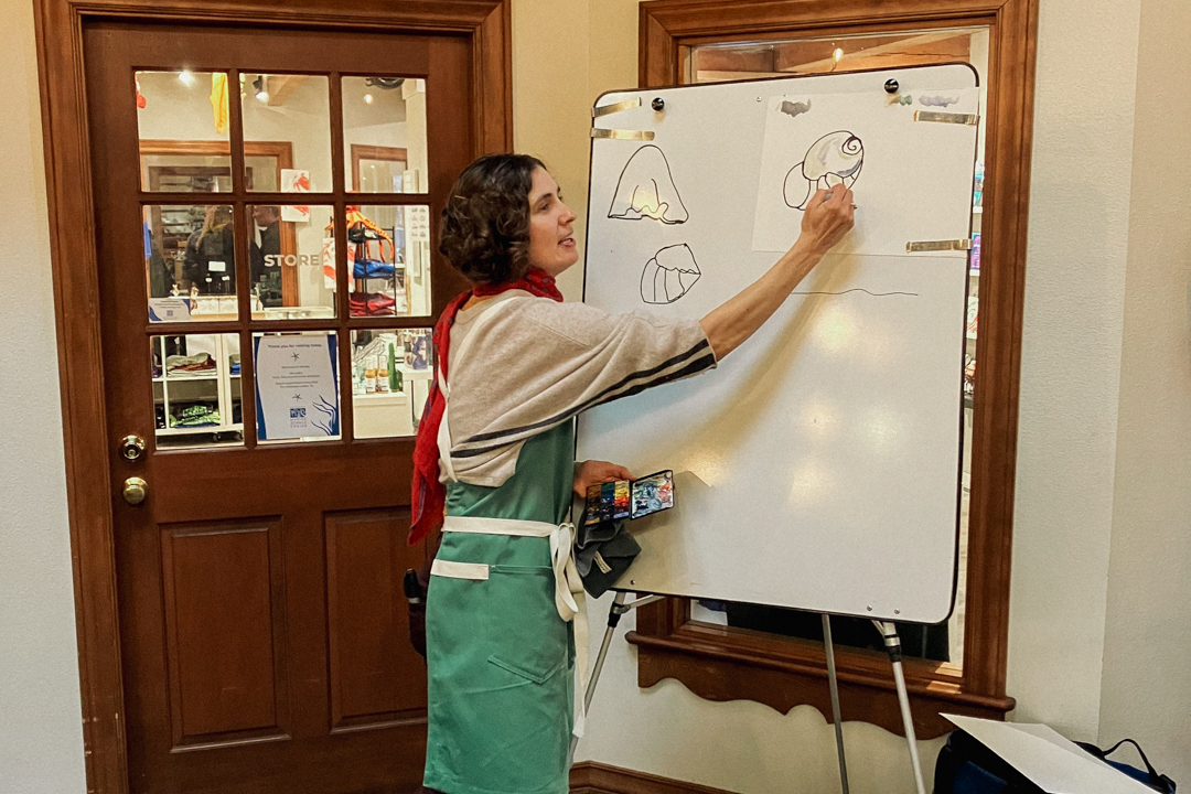 Person teaching a beginners drawing class using a white board to draw shapes.