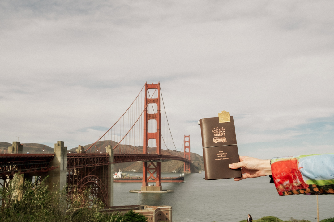 Person holding a TRAVELER'S notebook in front of the Golden Gate Bridge.