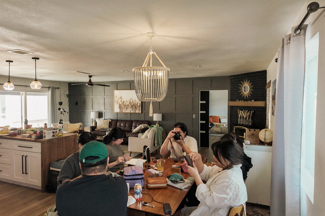 6 people journaling, crafting and taking photos at a large wooden dining table.