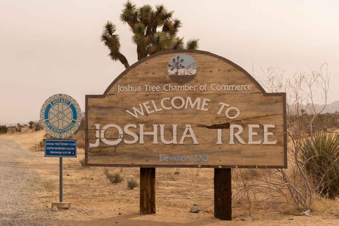 The "Welcome to Joshua Tree" sign on the side of a highway in the desert.