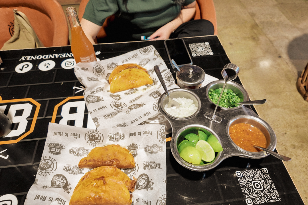 Two people eating Birria tacos on a black table filled with different condiments.