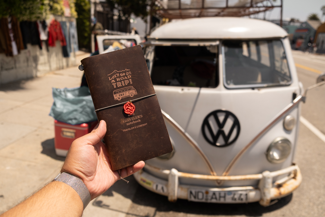 A person holding a Road Trip TRAVELER'S notebook in front of a VW Bus.