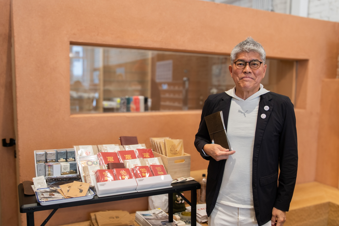 Mickey Kubota , president of JINS Eye-ware America, standing in front of the TRAVELER'S notebooks and related accessories at the TRC USA pop-up at JINS Abbot Kinney.