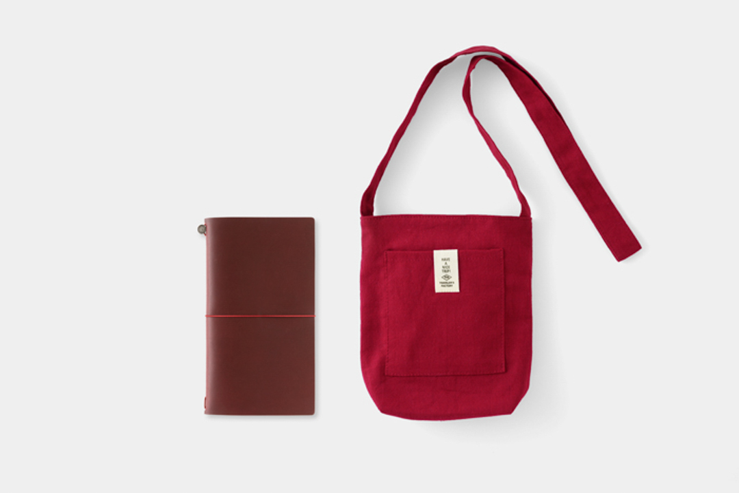 The LOVE AND TRIP red TRAVELER'S notebook beside the limited edition red sacoche bag.