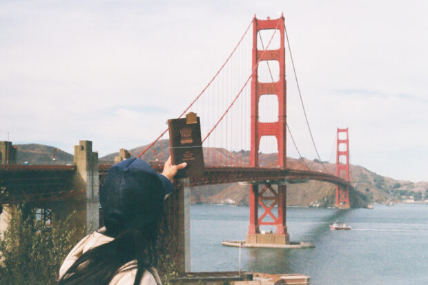 A person holding a TRAVELER'S notebook in front of the Golden Gate Bridge.