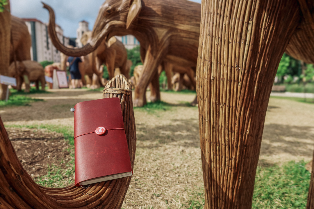 A red TRAVELER'S notebook resting on a wooden elephant sculpture.