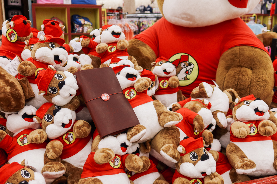 A red TRAVELER'S notebook amidst small Buc-ee's Beaver stuffed toys.
