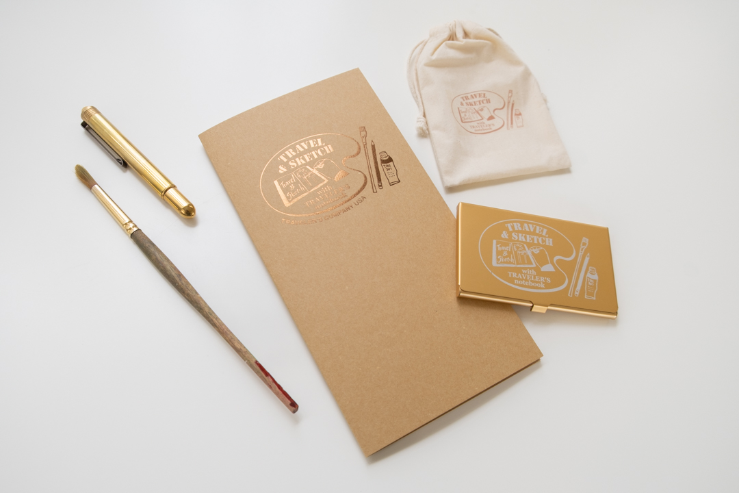 TRC USA Limited Accordion Fold Paper TRAVEL & SKETCH next to a pocket palette, a brass ballpoint pen, and a paint brush.