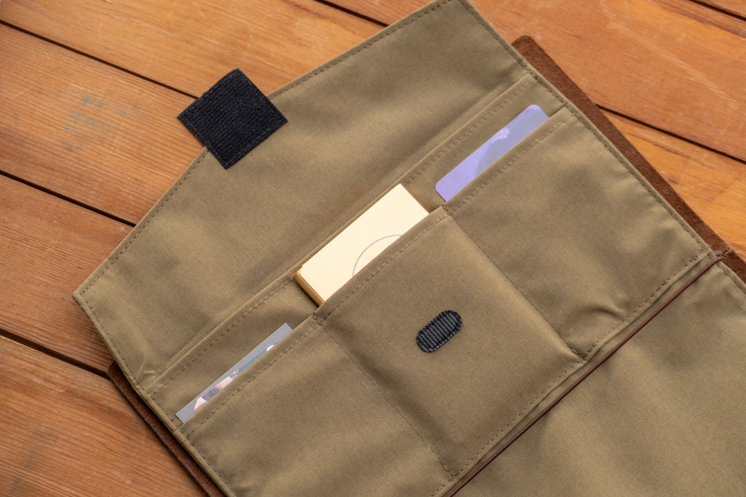 An olive TO&FRO TRAVELER'S notebook Zipper Case holding cards and a pocket palette.