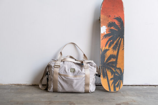 TO&FRO Boston Bag against a wall next to a skateboard.