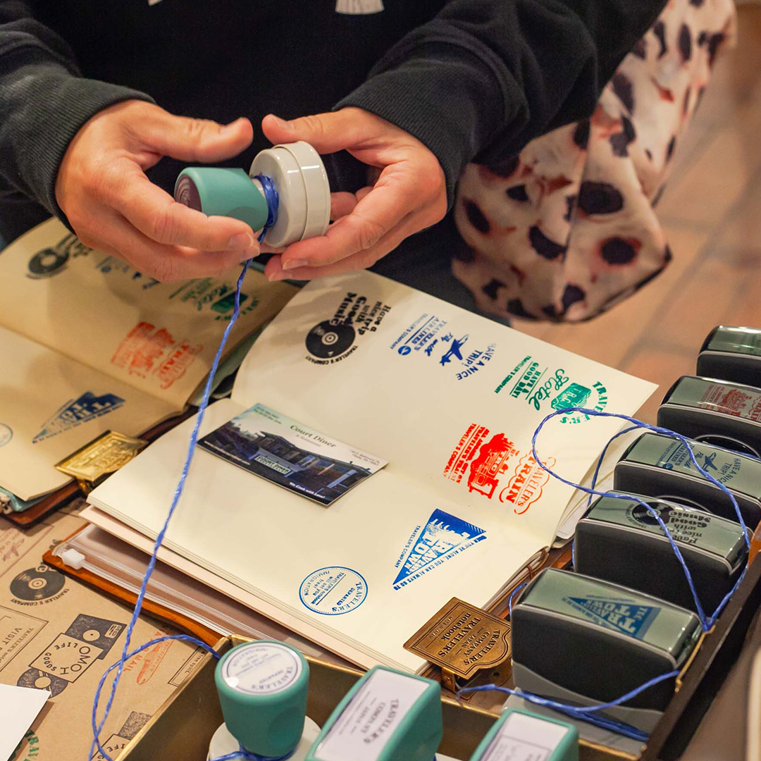 A person using the TRAVELER'S COMPANY stamp at OMOI's Stamp Caravan event.