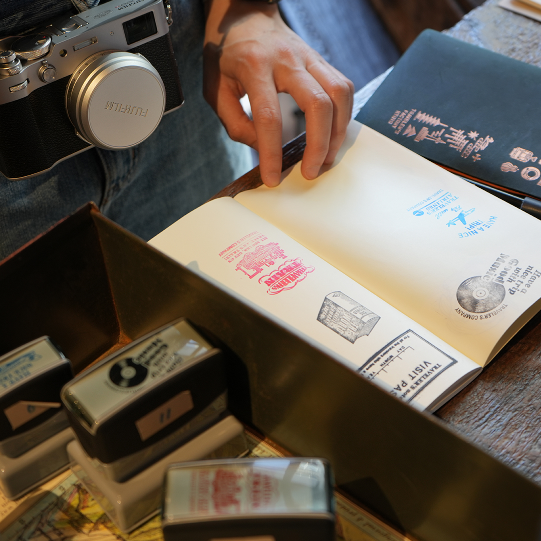 A hand holding open a TRAVELER'S notebook refill to collect stamps.